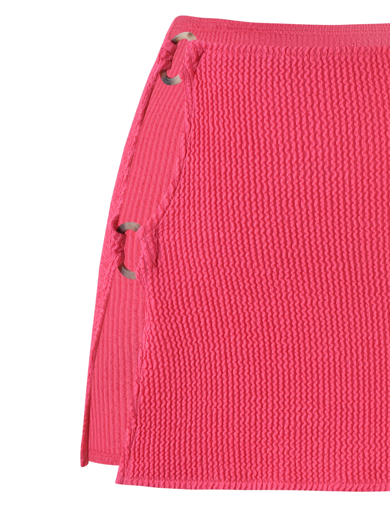 Close-up of the NEERA MINI SKIRT in Hot Pink Fuchsia by TIGERMIST, showcasing a bright pink, textured fabric. This high-waisted skirt features large silver grommets on one side, threaded with matching pink fabric. It boasts a unique side slit detail with an extra layer of fabric.