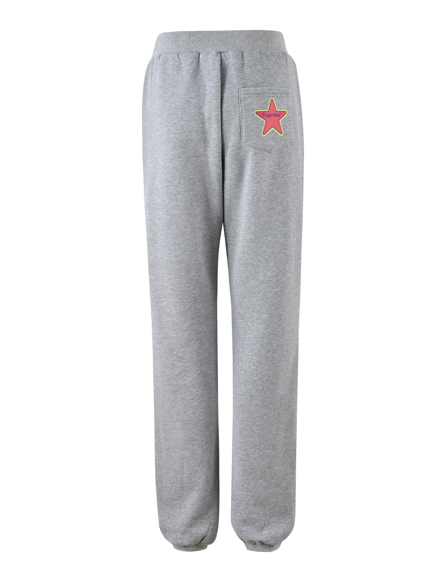 The LUMEN PANT - GREY by TIGERMIST features an elastic waistband and ankle cuffs. The back includes a pocket on the right side adorned with a red star patch outlined in yellow. The material is soft and comfortable.