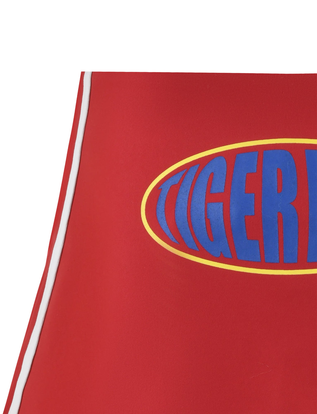Close-up of the red DELANEY SKORT - RED by TIGERMIST, showcasing the word "TIGER" in bold blue letters inside a yellow oval. Two white lines run parallel along the edge of this garment.