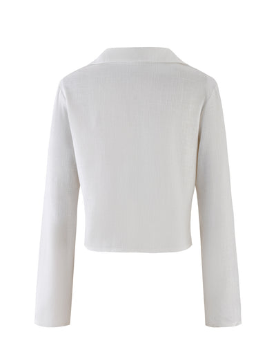 The image shows the back view of the AIDEN TOP - WHITE, a long-sleeve blouse from TIGERMIST. This cropped blouse features a collar and elegant design that rests above the waist. The lightweight fabric has a slightly textured finish, adding to its simple yet sophisticated look.