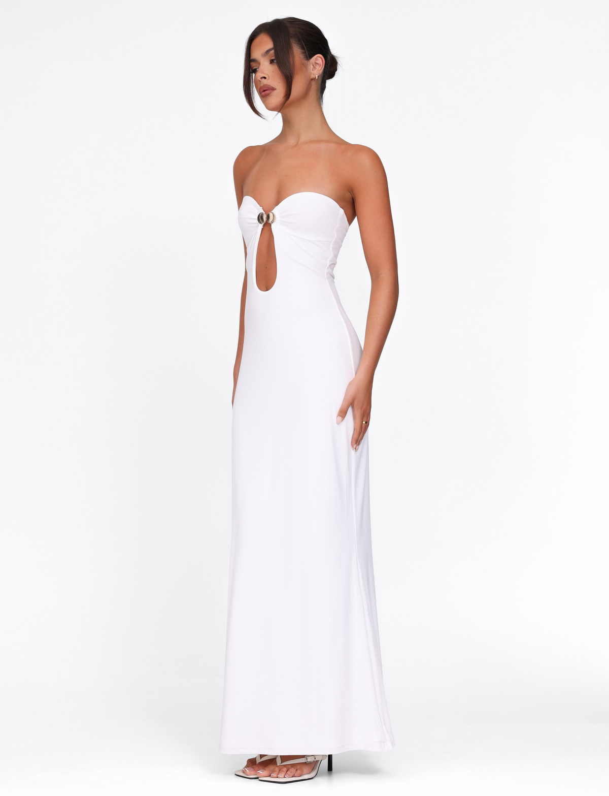 A woman in profile against a white background wears the TIGERMIST CECILY MAXI DRESS—an elegant, strapless, fitted white gown with a floor-length silhouette, front keyhole cutout, and ring detail.