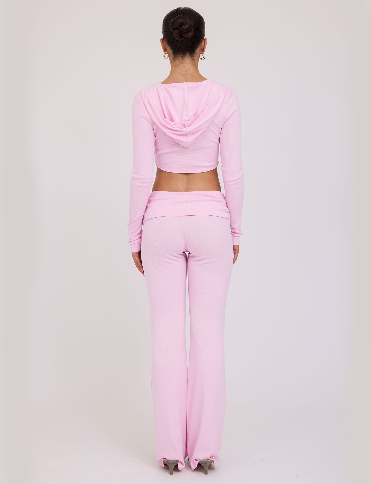 A person with hair in a bun is standing with their back to the camera, wearing a light pink TIGERMIST KARINA JUMPER and matching high-waisted, flared pants. The background is plain white.