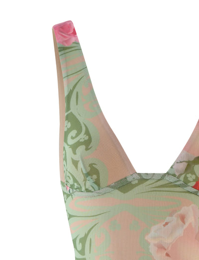 A close-up of the upper section of the LUNARIA DRESS - MULTI : MACRO FLORAL : SUMMER ROSE by TIGERMIST. The sleeveless dress features wide straps and an intricate design with green and pale pink floral patterns, including large blossoms and decorative foliage, all set against a beige background.