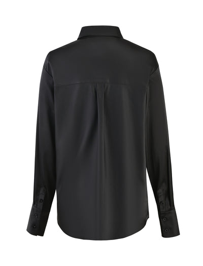 The image showcases the back view of the ALINA SHIRT - BLACK from TIGERMIST. This long-sleeved black shirt features a classic collar, button cuffs, and a back yoke with a pleat for added comfort and style. The fabric has a smooth, slightly shiny texture.