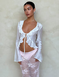 A person with dark hair poses against a plain background, wearing the CORVIN TOP - WHITE from TIGERMIST. They pair it with a pink lace skirt, look off to the side with a neutral expression, and hold their hands by their sides.