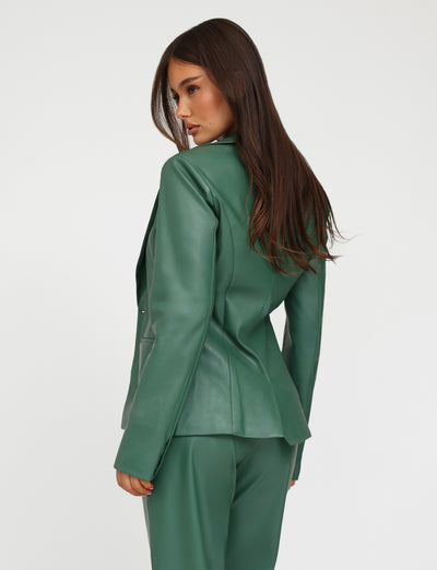 A woman with long, dark hair stands turned slightly to the side, looking down. She is wearing the MCKAY BLAZER - GREEN and matching pants from TIGERMIST. The background is plain white.