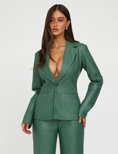 A woman with long brown hair and fair skin is wearing the MCKAY BLAZER - GREEN from TIGERMIST, complemented by matching trousers. The deep V-neckline of the blazer reveals a glimpse of a beige top underneath. She stands against a plain white background.