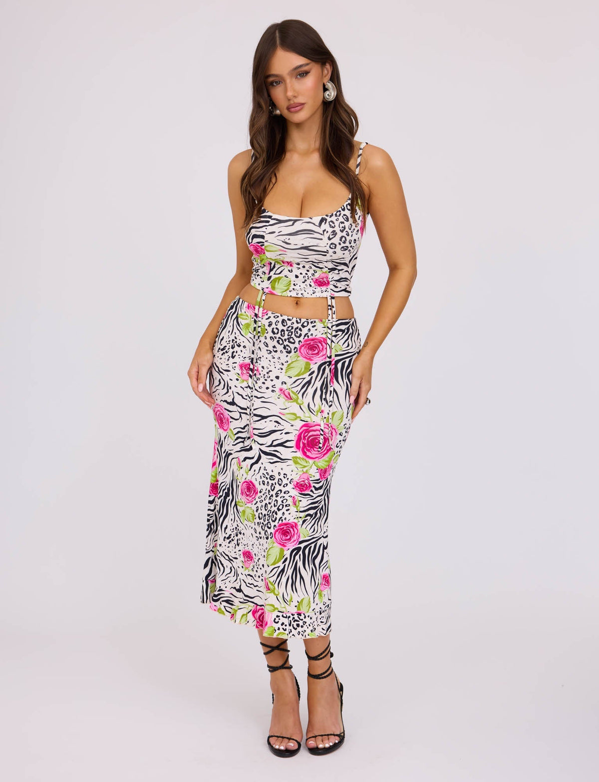 A woman is posing in the vibrant IRIE SKIRT - MULTI : ZEBRA from TIGERMIST, featuring a mix of zebra and leopard prints with vibrant pink and green floral patterns. She completes her look with black strappy high-heel shoes against a plain white background.