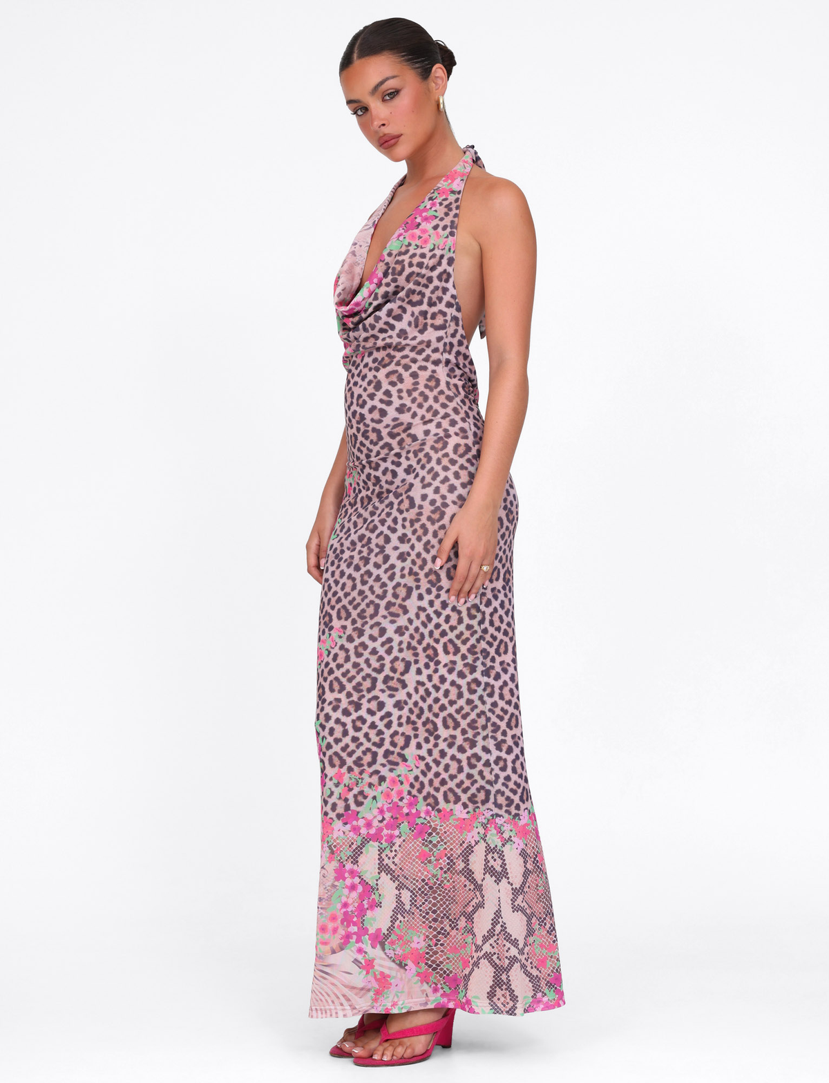 A woman models the TIGERMIST CATALINA MAXI DRESS in Neutral Animal Floral Border, a sleeveless halter style with pink and brown leopard floral print and snakeskin accents at the hem. She pairs it with pink heels against a white background.
