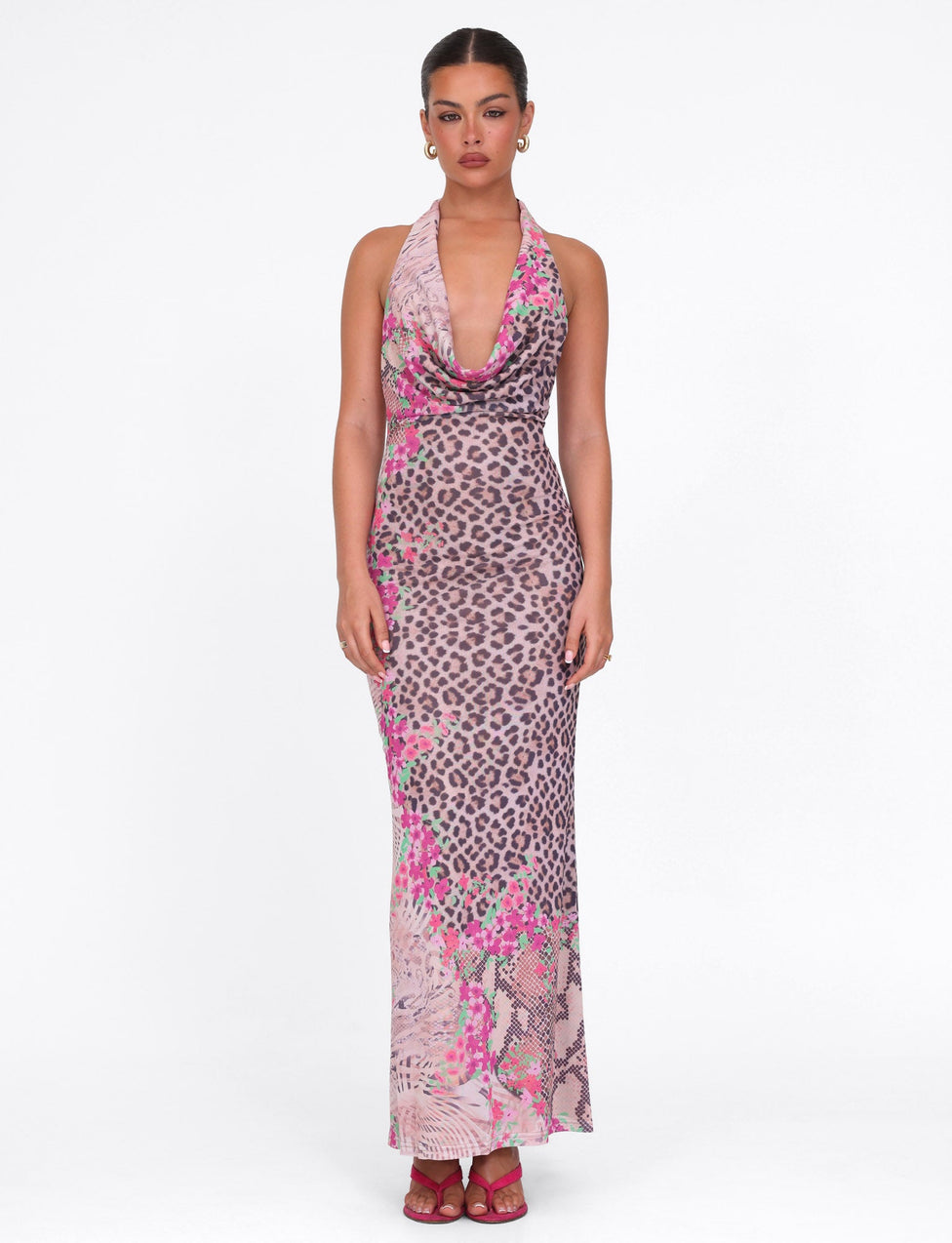 A woman faces forward in the TIGERMIST CATALINA MAXI DRESS - NEUTRAL : ANIMAL FLORAL BORDER, her hair pulled back and wearing pink heels, against a plain white background.