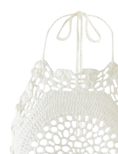 Close-up of the Maceline Dress in white from TIGERMIST. This dress features intricate crocheted patterns, showcasing an open floral-like motif crafted with delicate crochet threads, and it ties into a bow at the neck. The detailed and delicate crochet work highlights its exquisite craftsmanship.