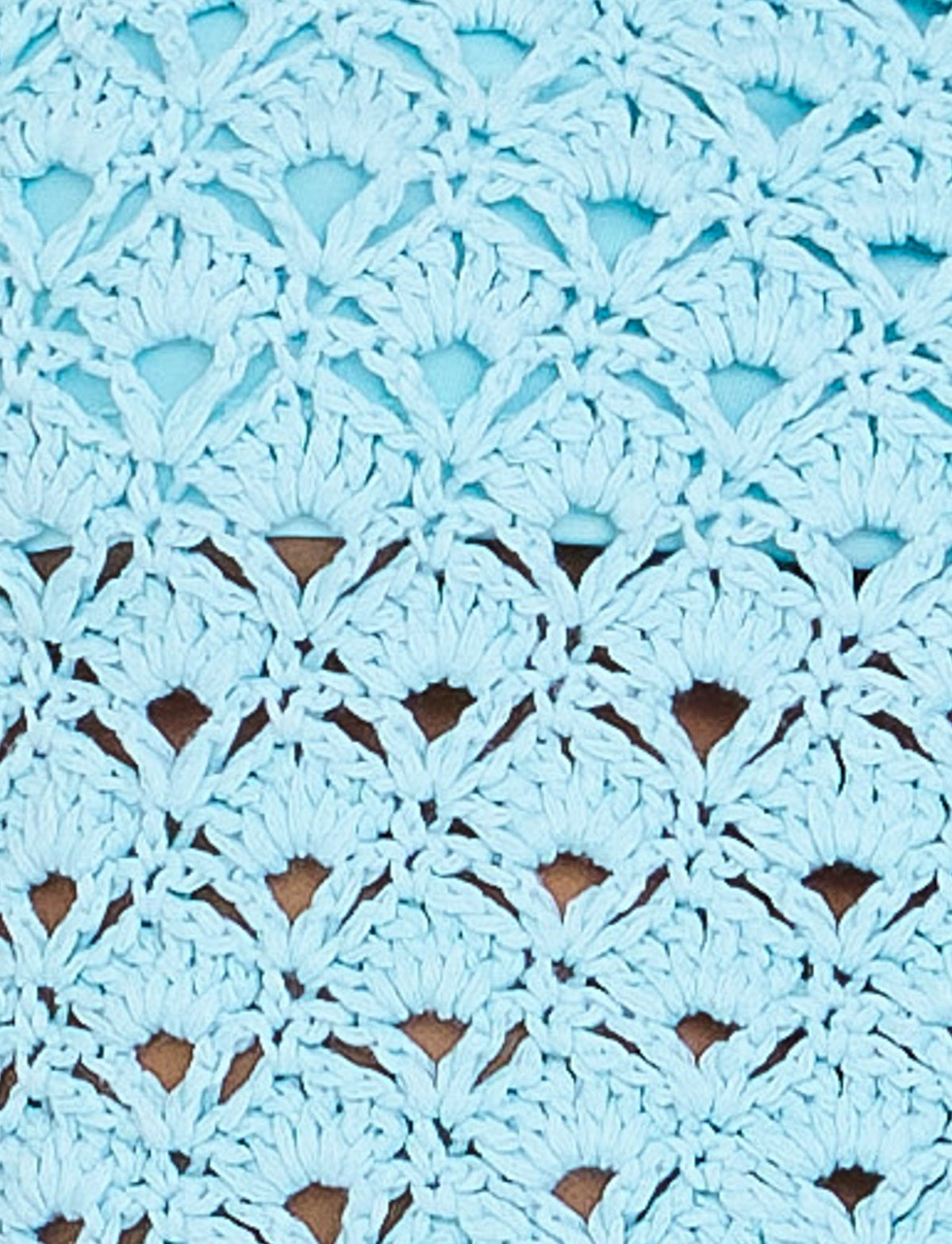 Close-up of the SUNNIVA BIKINI TOP in baby blue by TIGERMIST, featuring a light blue crocheted fabric with a scalloped, intricate pattern. The stitches form a series of repeating, semi-circular shapes, giving the bikini top a textured and airy look. The background color peeks through the open spaces of the crochet work.