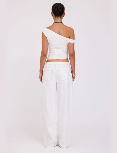 A person stands facing away from the camera, wearing the stylish KADENCE TOP in white and high-waisted wide-leg white jeans from TIGERMIST. Their hair is tied up in a bun, and they are accessorized with a necklace and bracelet. The background is plain white.