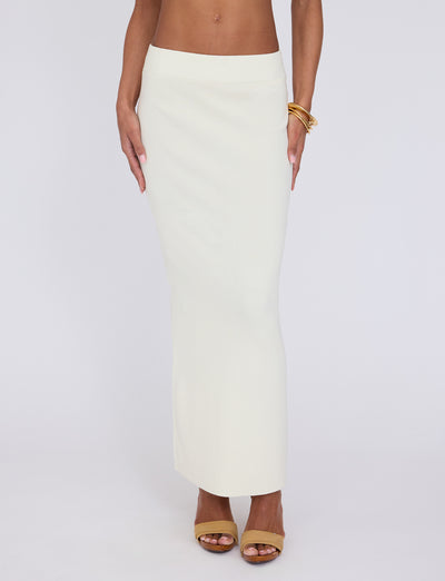 A person wearing the LEDGER SKIRT in white and cream from TIGERMIST, paired with tan open-toed high heels. They are accessorized with gold bangles on their wrist. The photo captures the lower half of the person, from the waist down, against a plain white background.