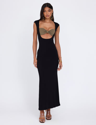 A woman stands confidently in the TIGERMIST BLAKELY DRESS - BLACK, a form-fitting, floor-length dress featuring a cut-out bodice with an olive green bandeau top underneath. She accessorizes with hoop earrings, a bracelet, and strappy heels against a plain white background.