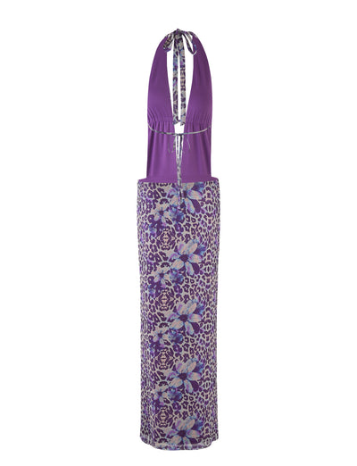The MAGDALENA MAXI DRESS - PURPLE by TIGERMIST, designed by Poppy Leopard, is a stunning halter-neck dress featuring a plunging neckline and keyhole detail. This dress showcases a fitted bodice and a long, straight skirt embellished with floral and abstract patterns in shades of purple, blue, and white.