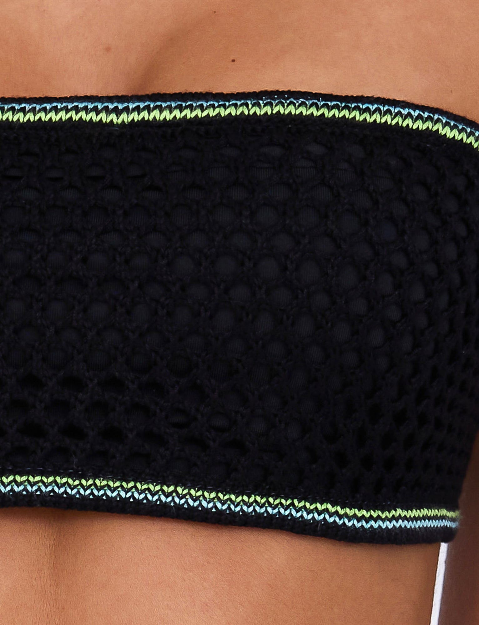 Close-up of a person wearing the AZARIA TOP - BLACK from TIGERMIST. The top features a textured knit pattern with blue and green trim at the top and bottom edges. The person's shoulders and upper chest are visible against a light background.