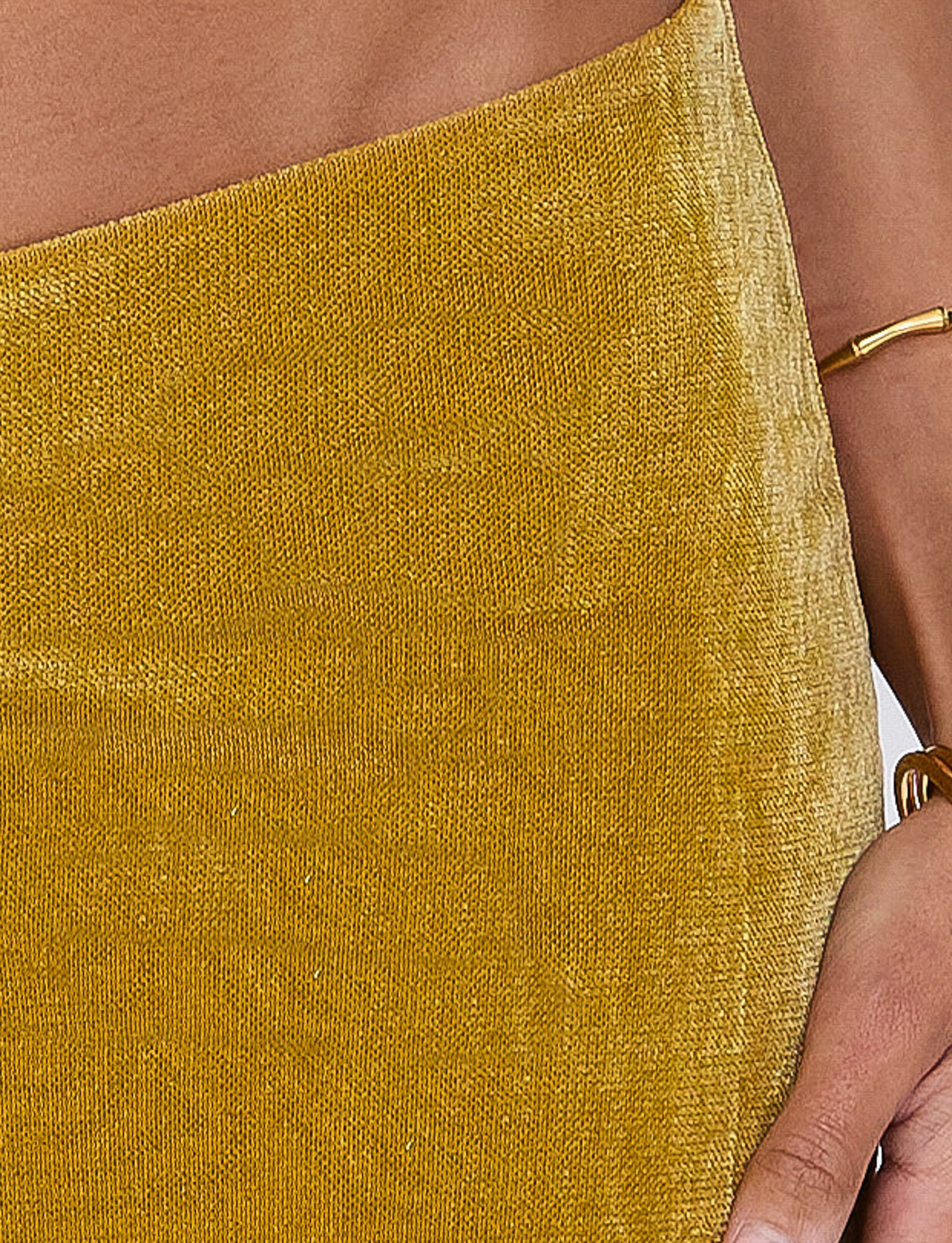 Close-up of a person in the HARLOWE SKIRT - GOLD by TIGERMIST. Their right hand, adorned with a gold bracelet, rests by their side. The skin is light brown.
