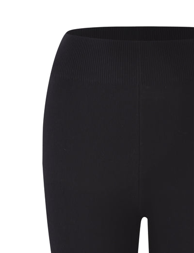 A close-up view of the upper part of a pair of TIGERMIST LEDGER CAPRI leggings in black. The high-rise waistband and smooth, stretchy fabric are prominently displayed, highlighting their bodycon fit around the top section of one leg.