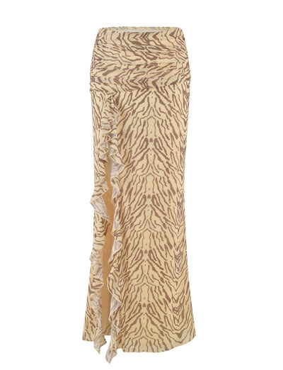 The RUMER SKIRT - YELLOW : ZEBRA by TIGERMIST is a high-waisted maxi skirt adorned with a beige and brown patterned design, showcasing an animal print in vibrant hues of yellow zebra. It features a wavy, ruffled trim running down the left side and exudes a stylish, flowing appearance against a plain white background.