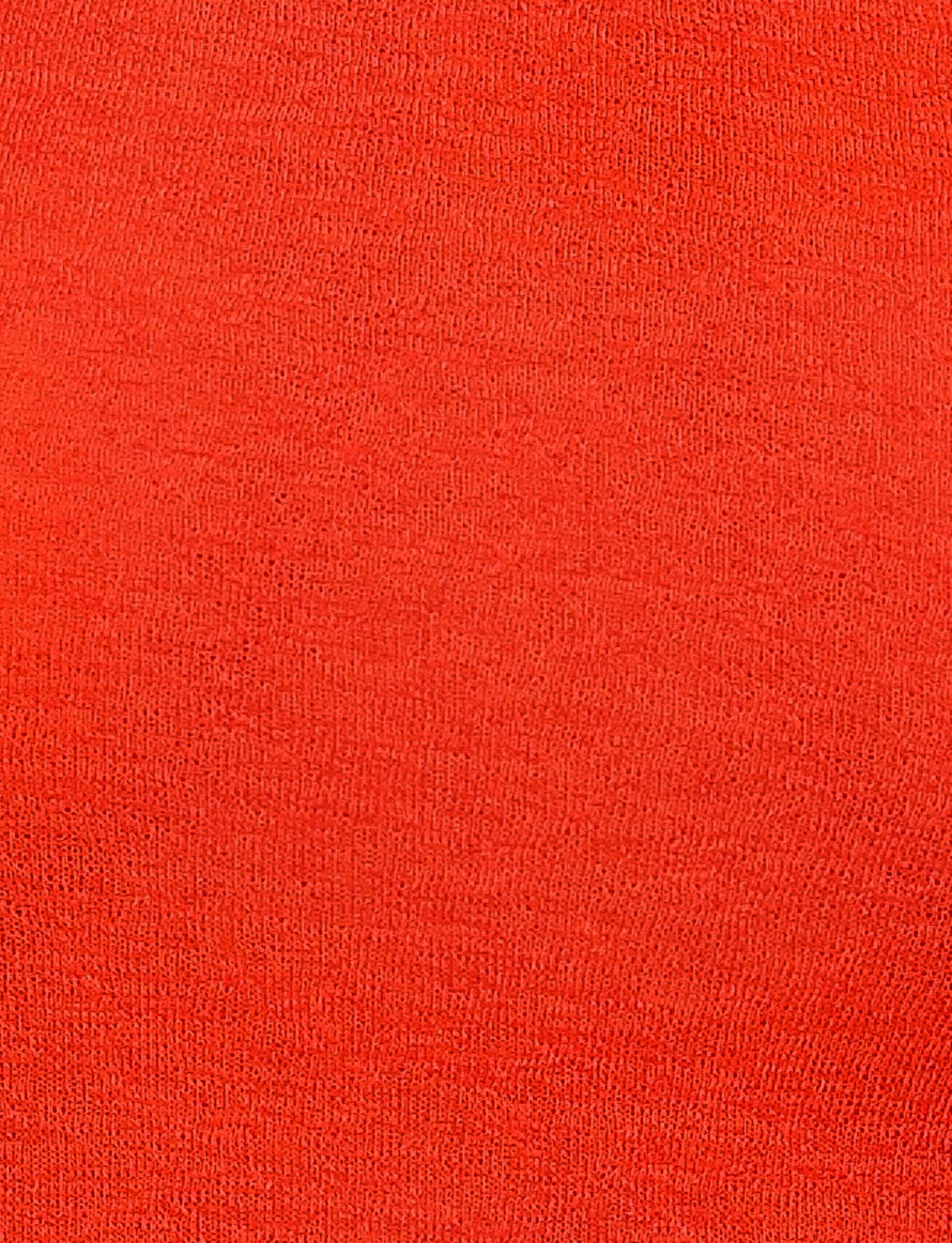 A close-up view of the BRYNA JUMPER - RED by TIGERMIST reveals a fabric with a plain red color. The texture appears soft and uniform, suitable for clothing or upholstery. This knit fabrication has no visible patterns or designs on the material, making it ideal for creating a classic red sweater with a fitted silhouette.