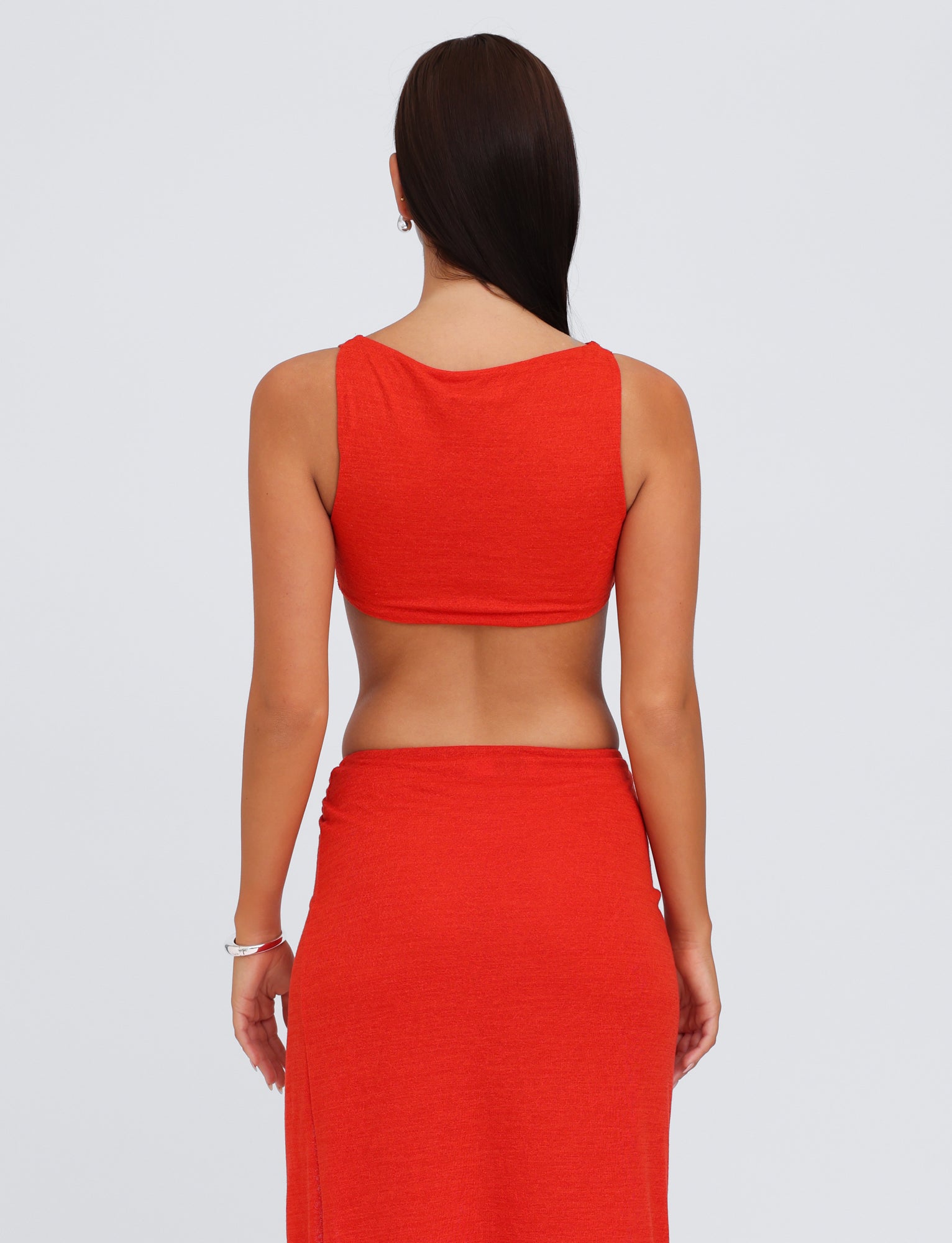 A person with long dark hair is standing with their back to the camera, wearing the TIGERMIST PAXTON TOP - RED : OMBRE, paired with a matching bodycon fit skirt. The background is a plain light color.