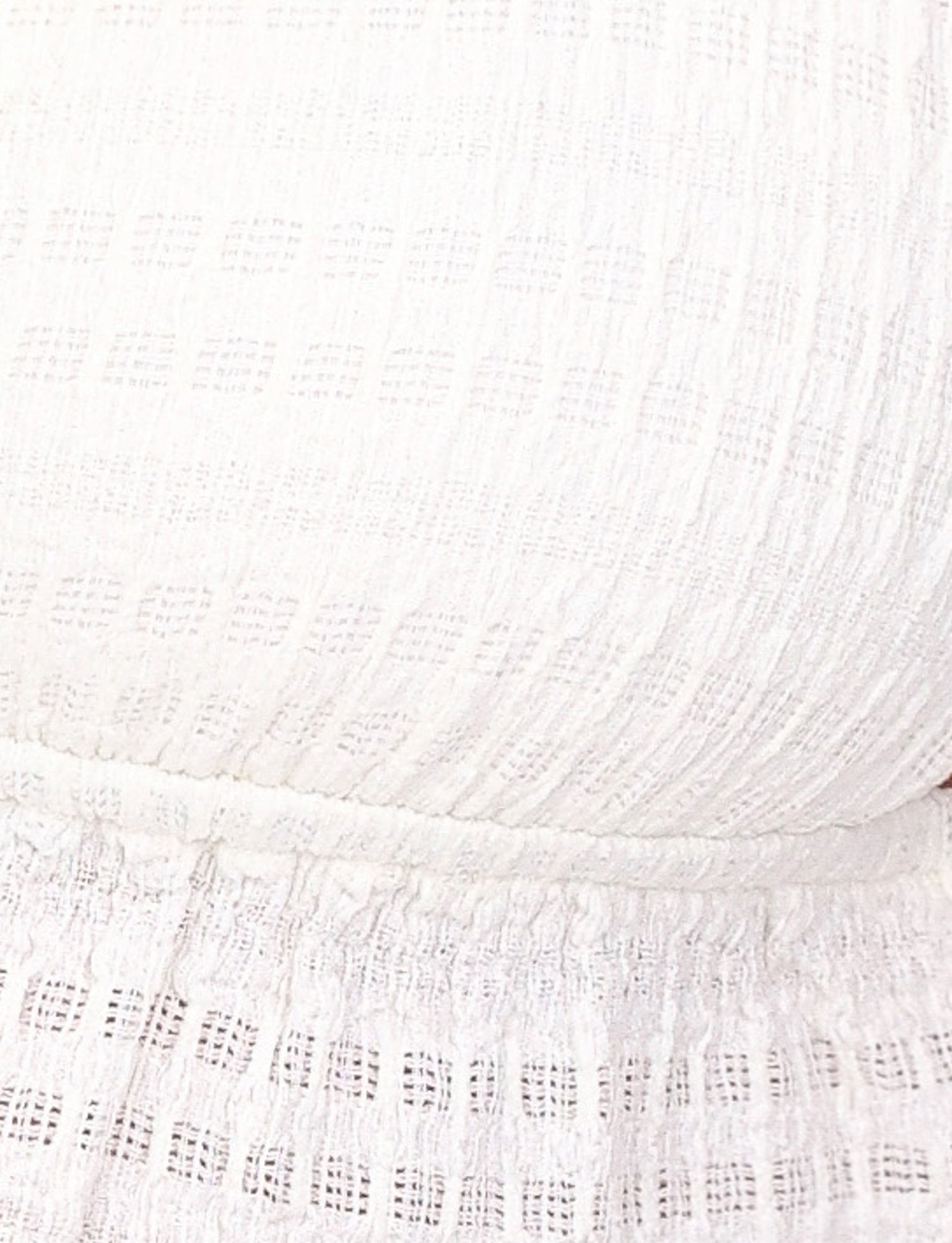 Close-up image of the ALDRIDGE TOP - WHITE by TIGERMIST, showcasing its white textured jersey fabric with a grid-like pattern. The material features a snug fit with gathered and slightly ruffled details near the bottom edge, resembling a crop-length camisole top.