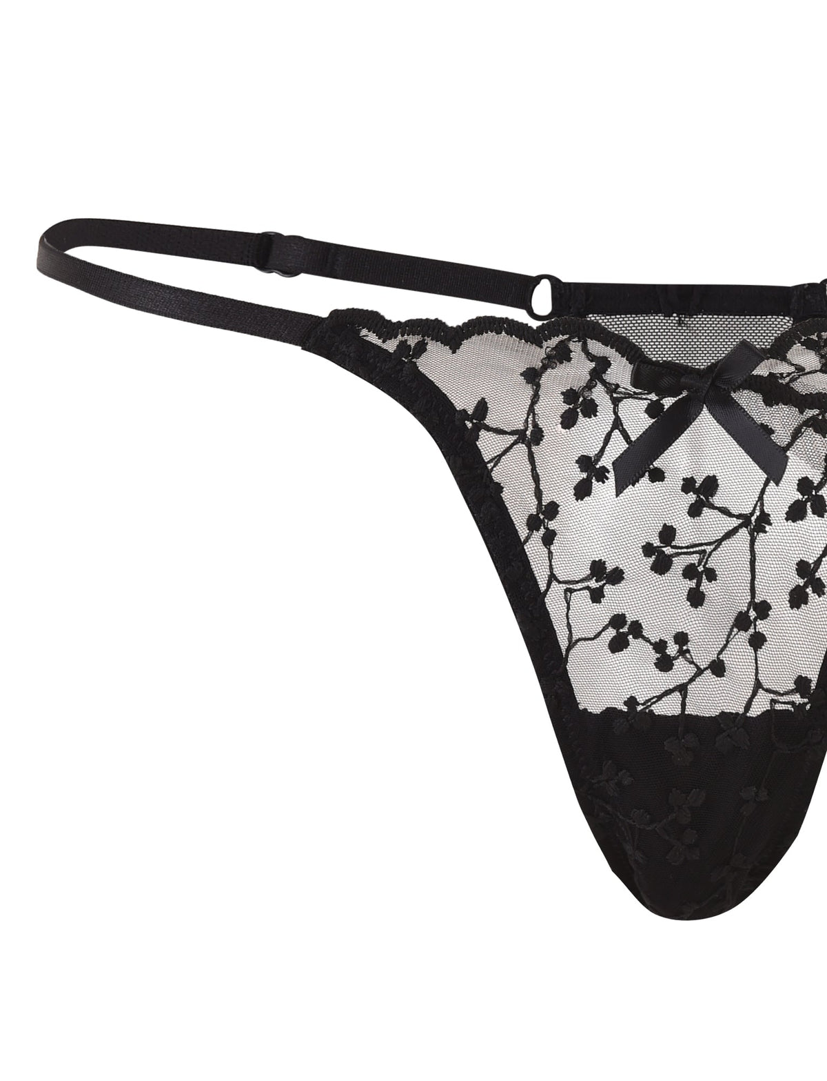 A close-up image of the TALIYAH SET - BLACK by TIGERMIST showcases a black lace thong adorned with floral embroidery. This thong features adjustable side straps and a small black satin bow at the center front. The intricate lace pattern imparts a delicate and elegant look, perfectly complementing its matching bra and g-string set.