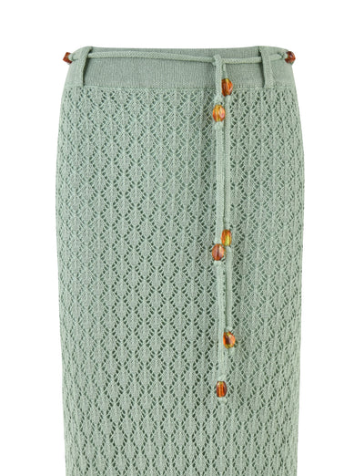 The COLLINA SKIRT - GREEN by TIGERMIST is a mint green, high-waisted maxi length crochet skirt with a diamond pattern and features a tie belt adorned with amber beads.
