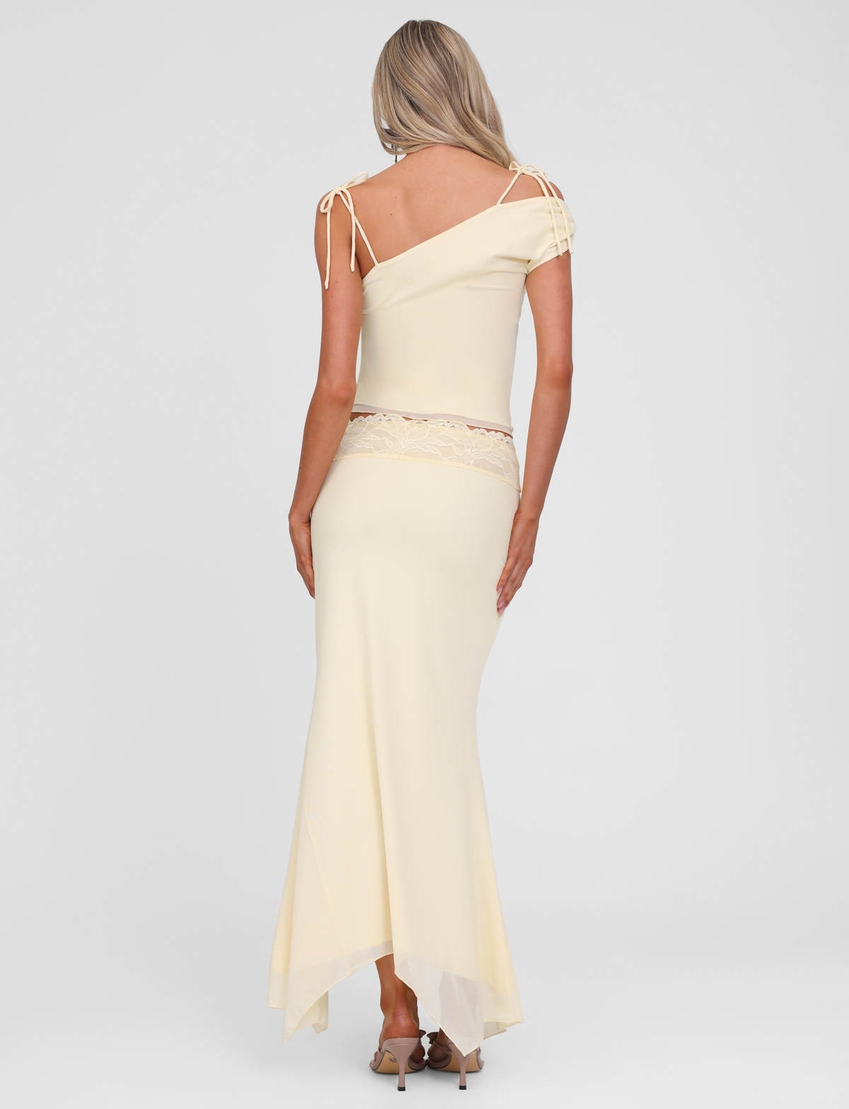 A woman with long blonde hair faces away, wearing the TIGERMIST LILLIAN SKIRT in yellow and beige heels, set against a plain white background.
