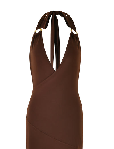 The MYLES DRESS - BROWN : CHOCOLATE by TIGERMIST is a stunning chocolate brown maxi dress featuring a sleeveless halter-neck design and plunging V-neckline adorned with gold o-ring details at the straps. This dress boasts a wrap-style bodice and a fitted silhouette, perfect for making a statement.