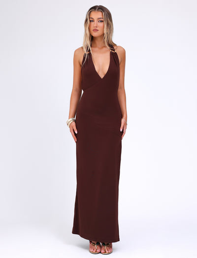 A woman stands against a plain white background, wearing the TIGERMIST MYLES DRESS in chocolate brown, showcasing its fitted silhouette and thin shoulder straps. She has long, wavy blonde hair and complements her look with gold o-ring details, bracelets, and rings. She gazes directly at the camera.