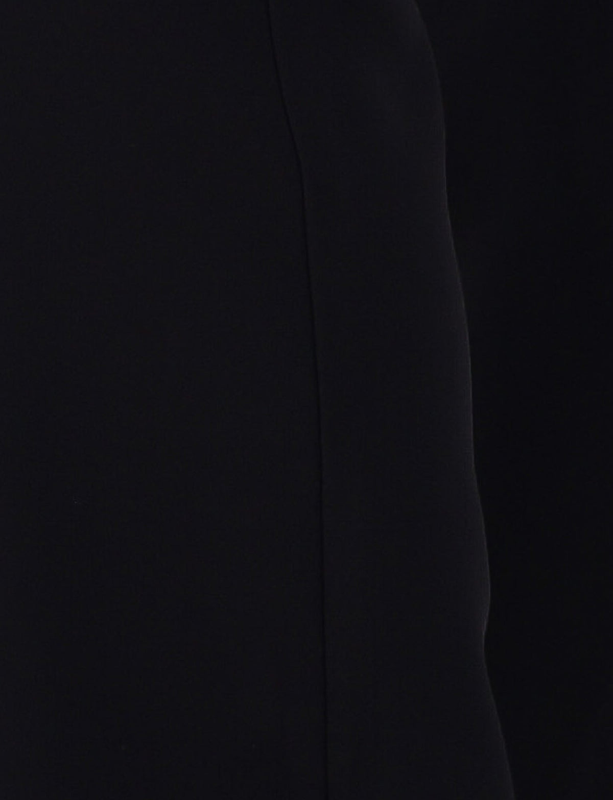 Close-up of the TERLA PANT - BLACK by TIGERMIST, showcasing its smooth, sleek black fabric with a vertical seam down the middle. The slightly curved fabric on the right side creates a subtle shadow effect, suggesting a flared silhouette.