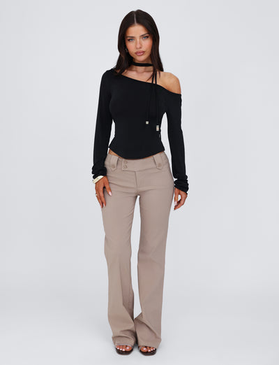 A woman with long dark hair is wearing a stylish TIGERMIST MIETTA TOP - BLACK, characterized by its one-shoulder design with a choker-style strap, paired with beige wide-leg pants made from high-stretch fabric. She stands against a plain white background, looking directly at the camera.