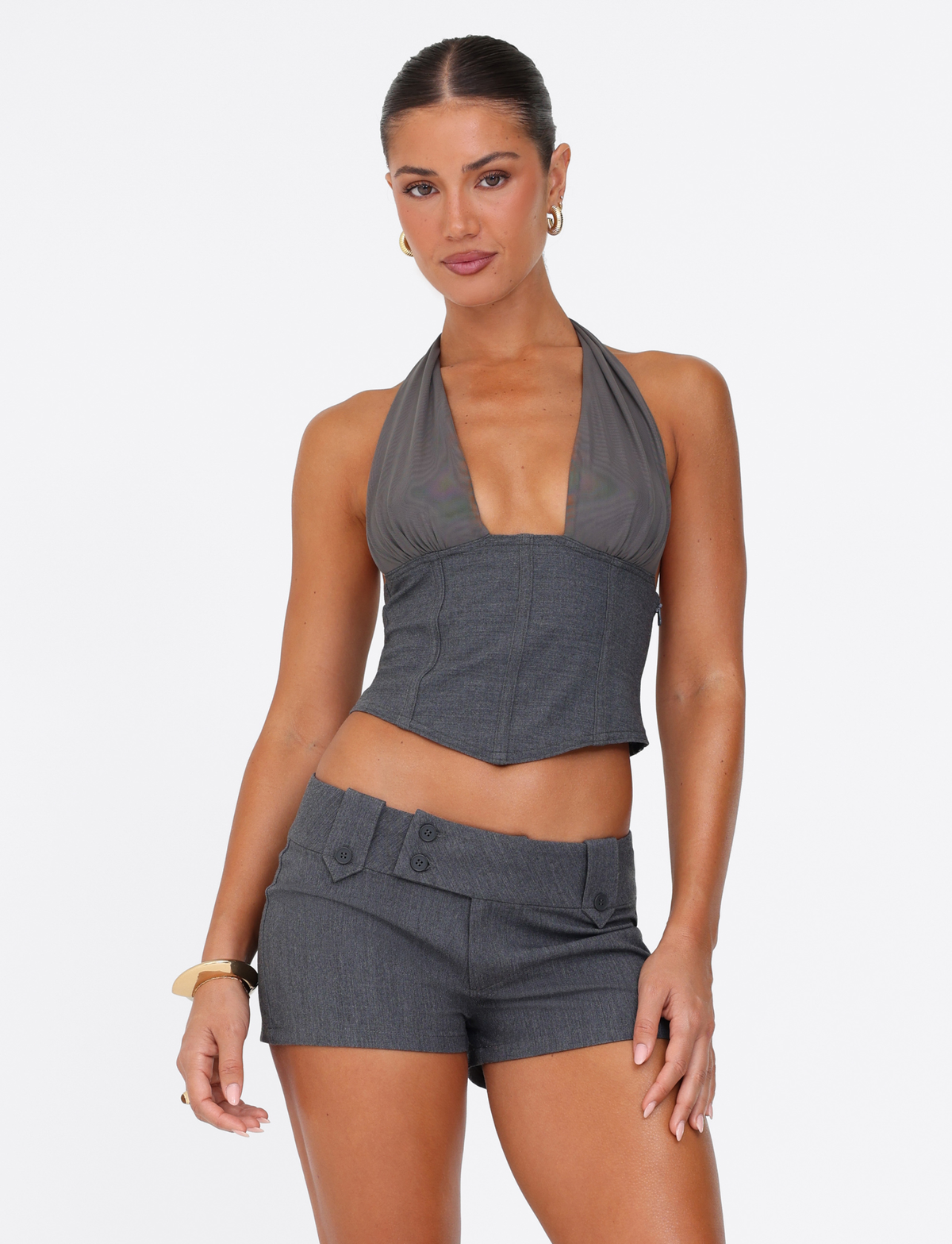 A woman stands against a white background, wearing TIGERMIST's KITTIE SHORT - GREY with a matching sleeveless deep V-neck top. Her hair is pulled back and she accessorizes with hoop earrings and bracelets.