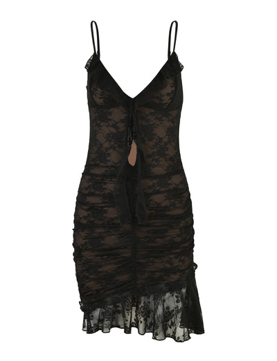 The CARLY LACE DRESS - BLACK by TIGERMIST showcases sheer fabric, adjustable shoulder straps, ruched sides, and a deep V-neckline. The dress also includes a tied front detail and a knee-length hem adorned with lace trim for a delicate and elegant look.