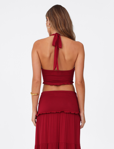A woman with long brown hair faces away from the camera against a plain white background, wearing the TIGERMIST KATYA HALTER TOP in red.
