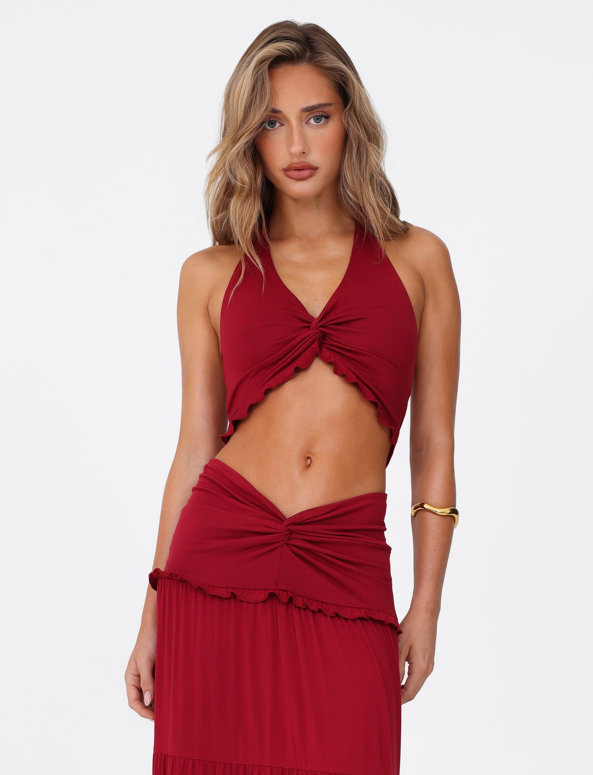 A woman with wavy blonde hair wears the TIGERMIST KATYA HALTER TOP in red, paired with a matching skirt. She stands against a plain white background, looking directly at the camera with a neutral expression.
