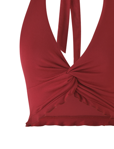The KATYA HALTER TOP - RED by TIGERMIST is a sleeveless crop halter top in deep red, featuring a twisted front knot and a subtle ruffled hem.
