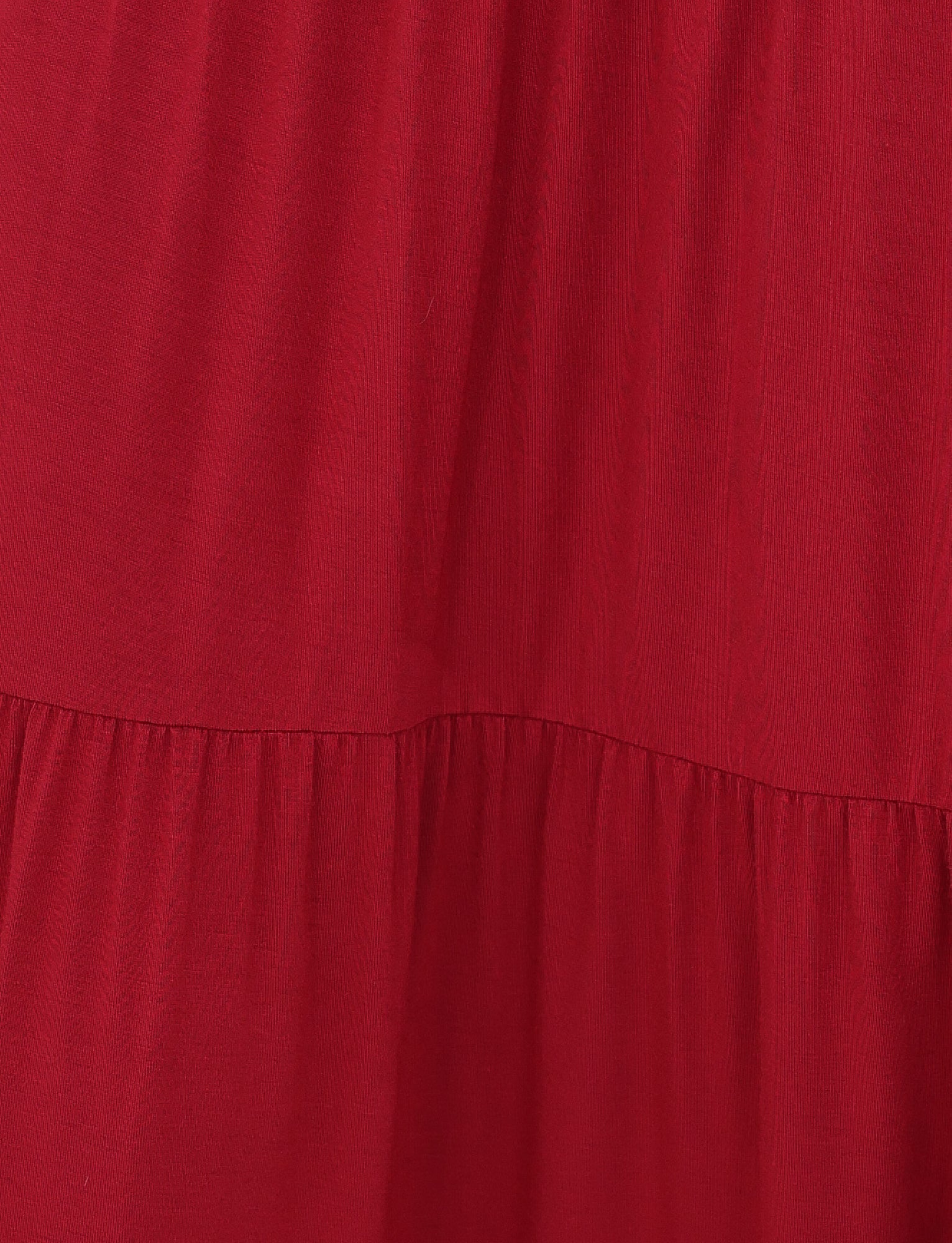 The KATYA MAXI SKIRT by TIGERMIST features a close-up of red gathered pleats creating soft, flowing folds. The high-stretch fabric offers a smooth appearance with a slight shine, suggesting a gentle, relaxed drape.