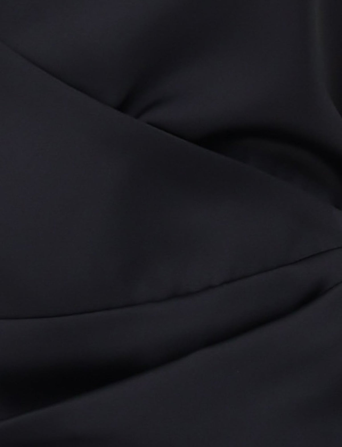 Close-up of the DAPHNIE SKORT - BLACK by TIGERMIST, featuring black fabric with diagonal seams that create a folded effect. The smooth, slightly shiny material conveys a formal or elegant texture, while the mini-length design introduces a modern flair.