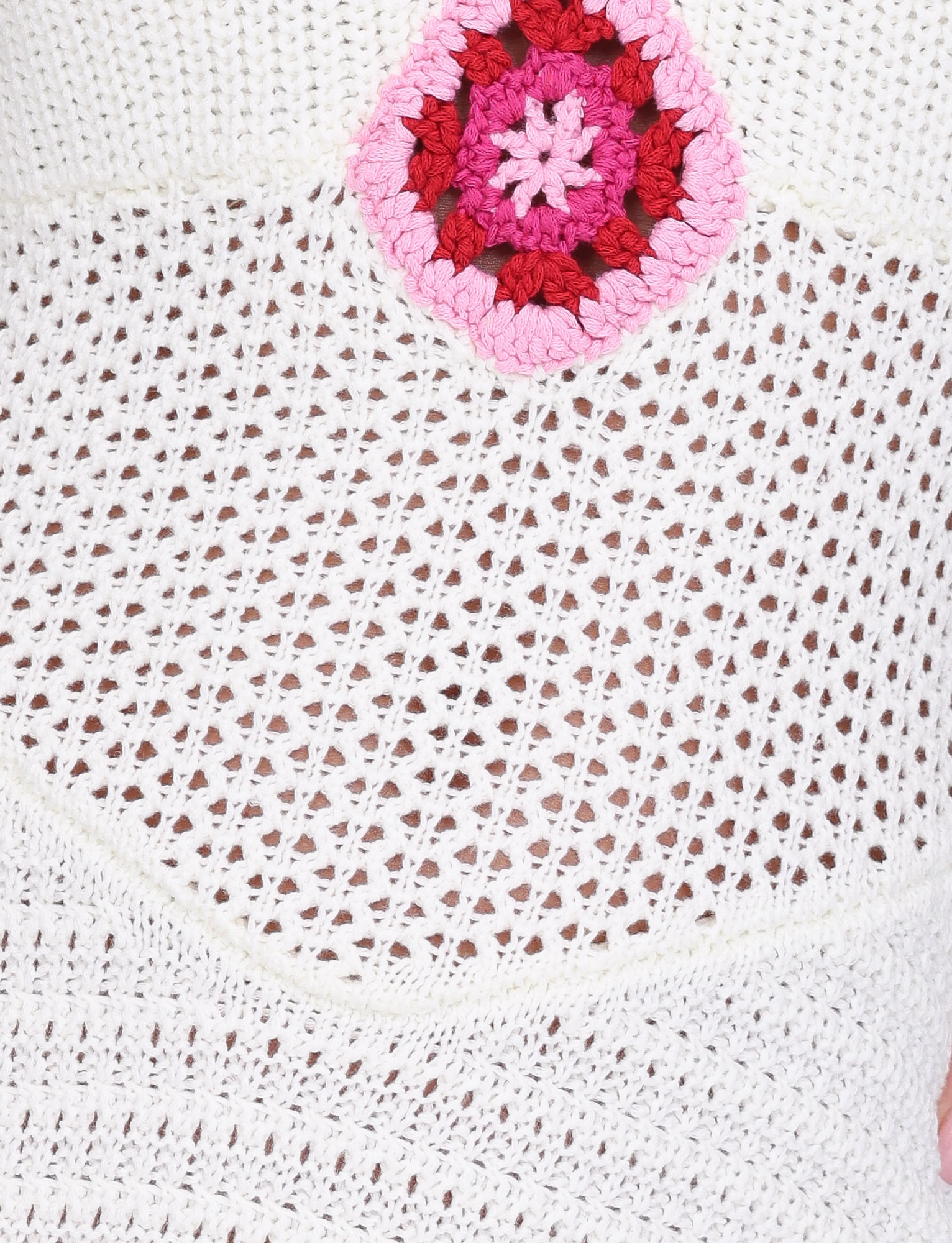 Close-up of the TENZIN MINI DRESS - CREAM by TIGERMIST, featuring airy white crochet fabric and a standout pink and red granny square patch near the top.