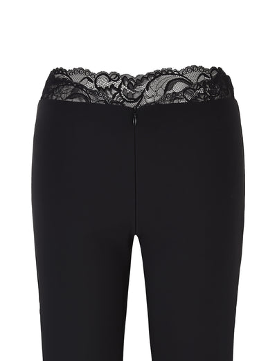 The NYOMI PANT - BLACK by TIGERMIST are black flared leg pants with a high waist and lace trim at the top, made from high stretch fabric and featuring a rear zipper closure.