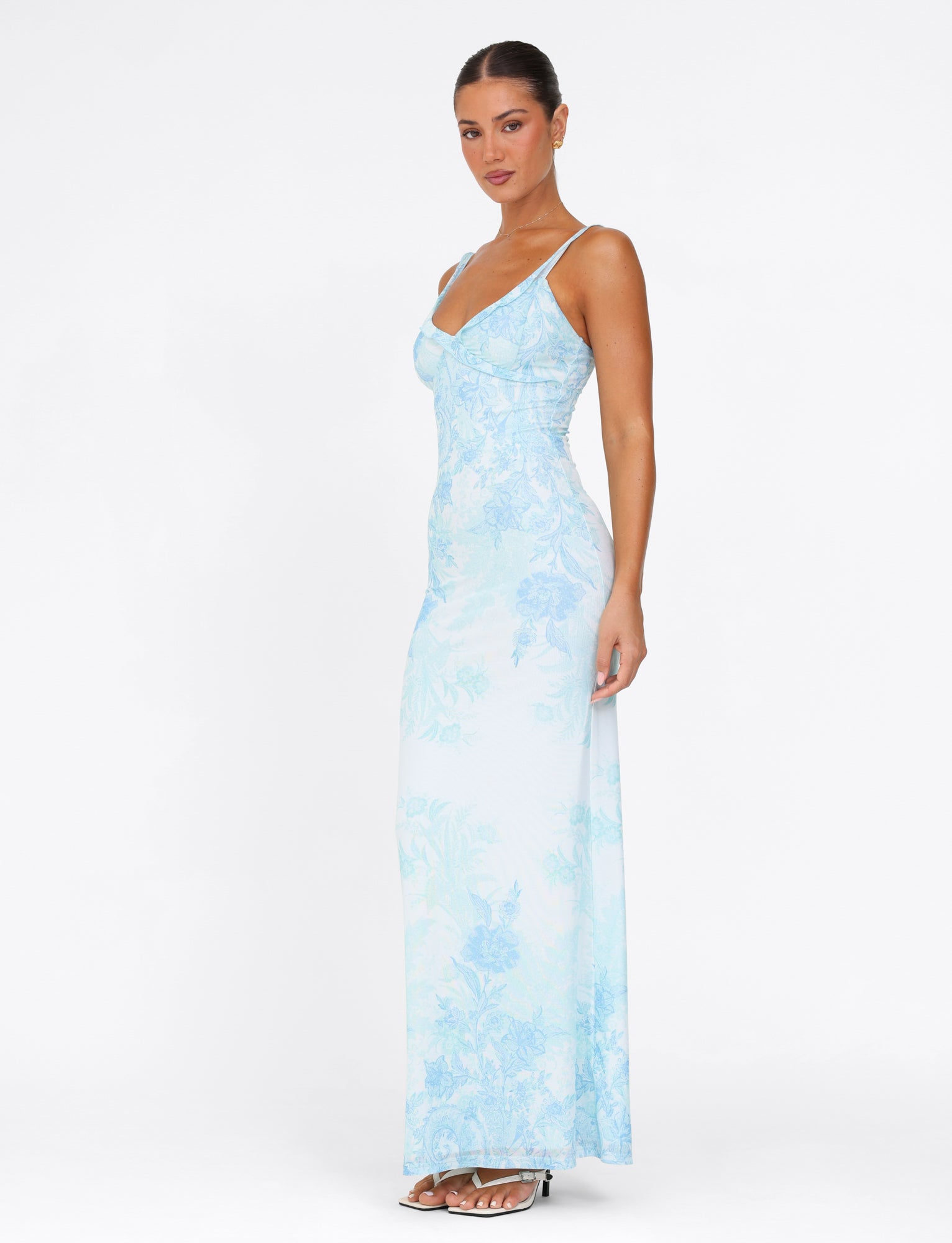 A woman gracefully poses in the TIGERMIST GUILIANNA FRILL MAXI DRESS - BLUE : FLORAL : TAPESTRY against a plain white background. This dress, made from high stretch fabric, showcases adjustable frill shoulder straps as she looks toward the camera, one leg slightly forward to highlight its elegant fit.