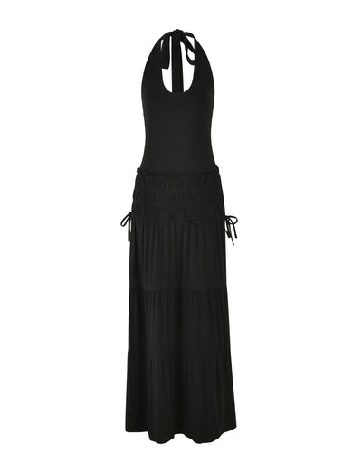 The DENALI HALTER MAXI DRESS - BLACK by TIGERMIST features a sleeveless design with a halter neck and a tiered skirt. It has a fitted top crafted from buttery jersey fabric, along with drawstring waist details that allow it to flow elegantly to the floor.