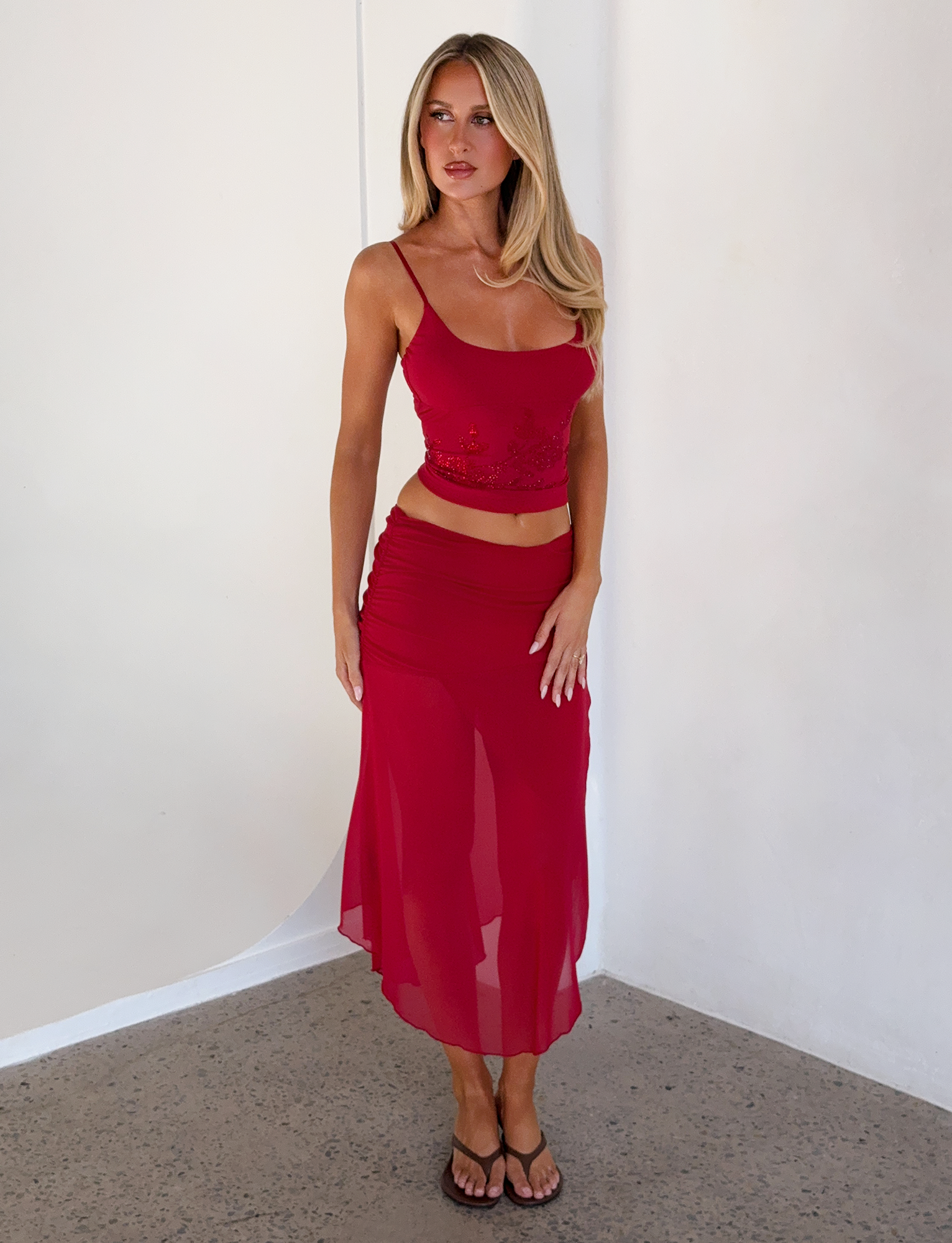 A woman wears the OCTAVIA TOP in red by TIGERMIST, featuring delicate floral embellishments.