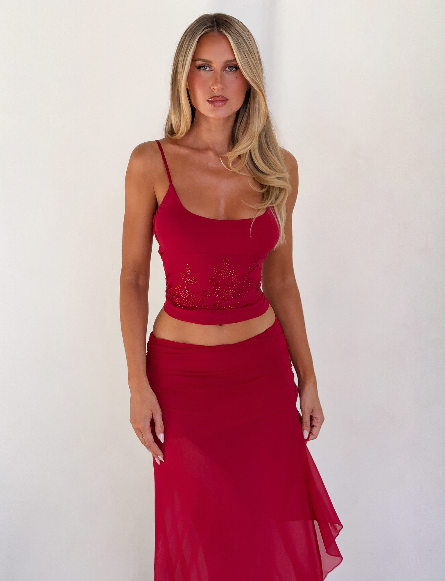 A woman with long blonde hair stands against a white background, wearing a fitted sleeveless red top and the TIGERMIST MARIANA SKIRT - RED with a ruched waistband. She has a neutral expression and her arms rest at her sides.