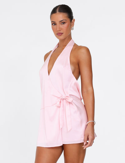 A woman is dressed in the TIGERMIST MONROE 2.0 MINI DRESS in pastel pink, echoing the elegance of a classic Monroe Dress with its halter-neck and wrap design, complete with a tied waist. Her hair is pulled back as she poses against a plain white background.