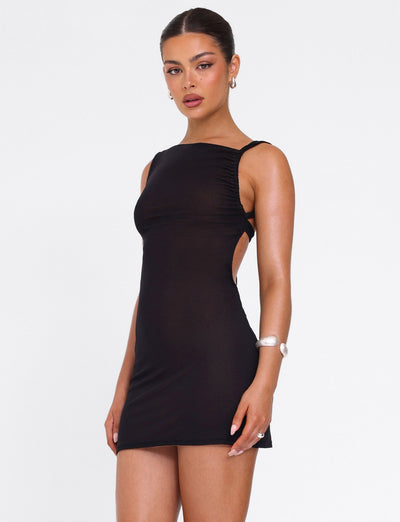 A woman models the TIGERMIST FREYA DRESS - BLACK, a buttery soft mini with adjustable asymmetrical neckline and side cutouts. She stands against a white background, hair pulled back, styled with hoop earrings and a bracelet.