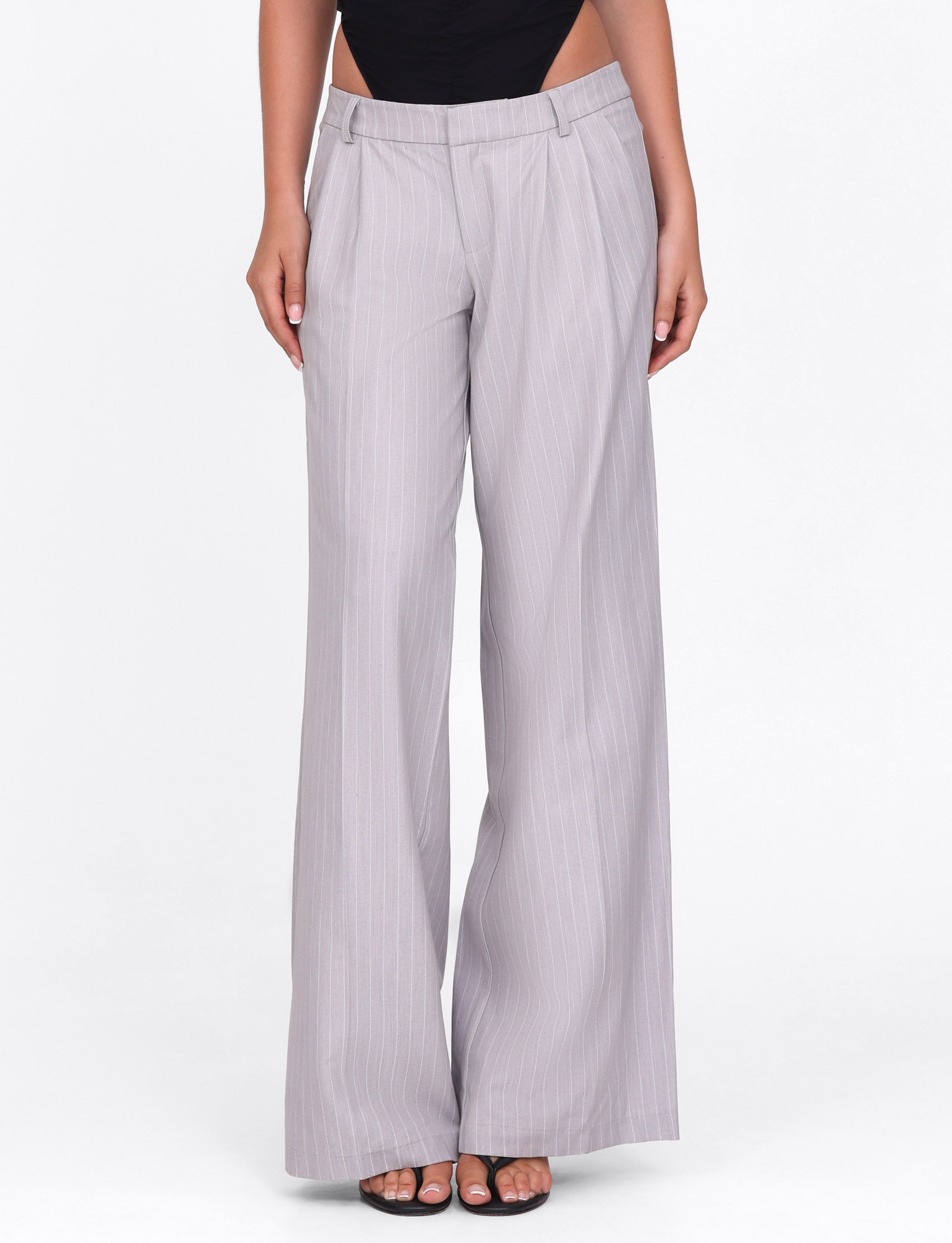 A model wears TIGERMIST's AMBERLY SUIT PANT in grey pinstripe, a high-waisted wide leg tailored pant, styled with black open-toed heels and a black top, shown from waist to feet on a plain white background.